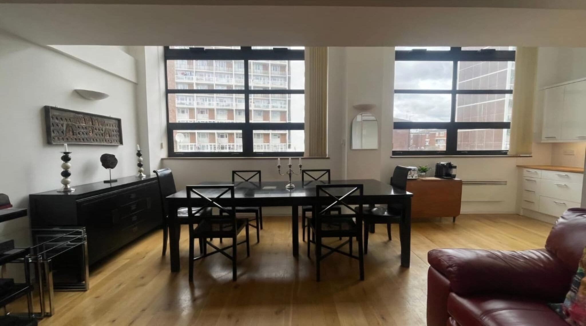 A modern living room with a dining area, large windows, a fireplace, and a kitchen area.