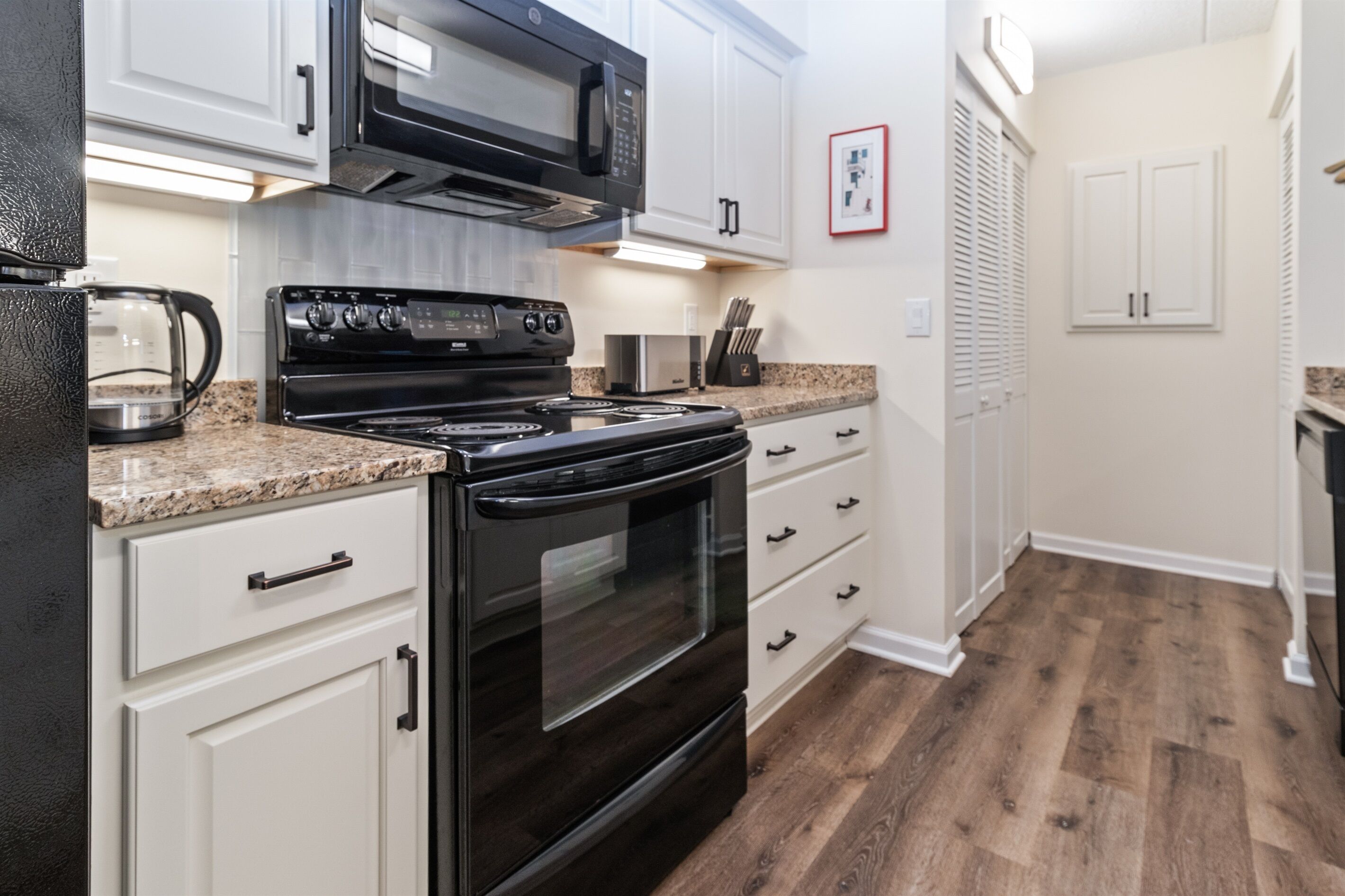 A kitchen with white cabinets, a black stove, and granite countertops.