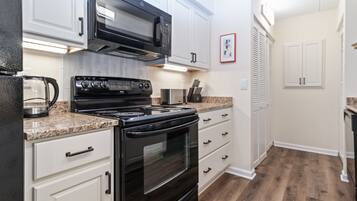 A kitchen with white cabinets, a black stove, and granite countertops.