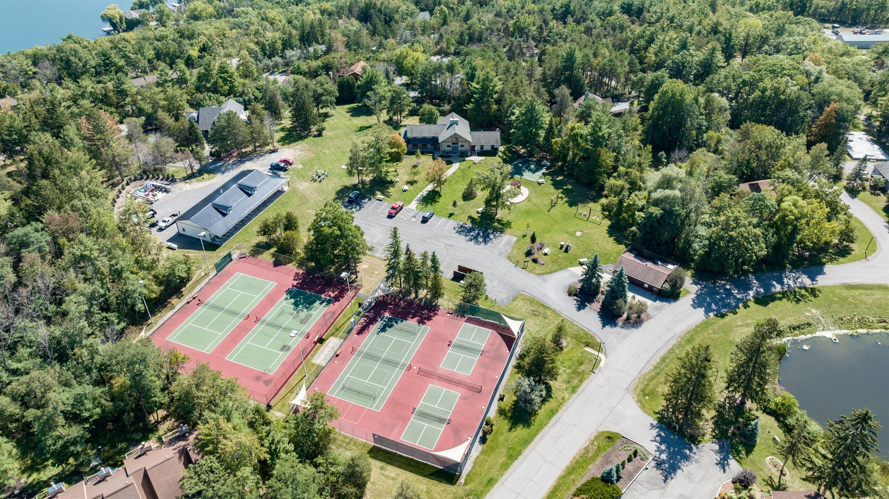An aerial view of a residential area with a tennis court, houses, and a lake.