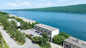 A multi-story hotel with a parking lot, surrounded by trees and a lake.