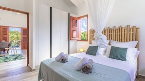 Ein Hotelzimmer mit einem großen Bett, einem hölzernen Kopfteil und Blick ins Freie durch eine geöffnete Tür.