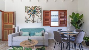 Ein Wohnzimmer mit einer Couch, einem Esstisch mit Stühlen, einem Couchtisch und einer großen Pflanze.