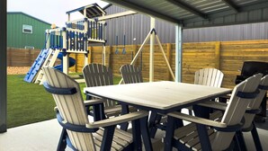 An outdoor patio area with a wooden table and chairs, a swing set, and a slide. - Fish Stories 5 Bedroom/3.5 Bathroom With Pool and Playscape (Port O'Connor)
