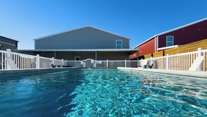 A swimming pool with a clear blue water surface, surrounded by white fences and buildings with a simple, modern architectural style. - Fish Stories 5 Bedroom/3.5 Bathroom With Pool and Playscape (Port O'Connor)