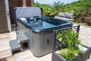 Un bain à remous doté d’un siège intégré et d’une petite table, entouré d’une végétation luxuriante et agrémenté d’un canapé d’extérieur confortable.