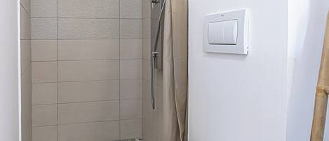 Un baño con ducha, inodoro e interruptor de luz en la pared.
