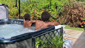 A hot tub with two people enjoying the view of a lush garden.