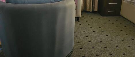 A hotel room with a sofa, a chair, a bed, a nightstand, and a lamp.