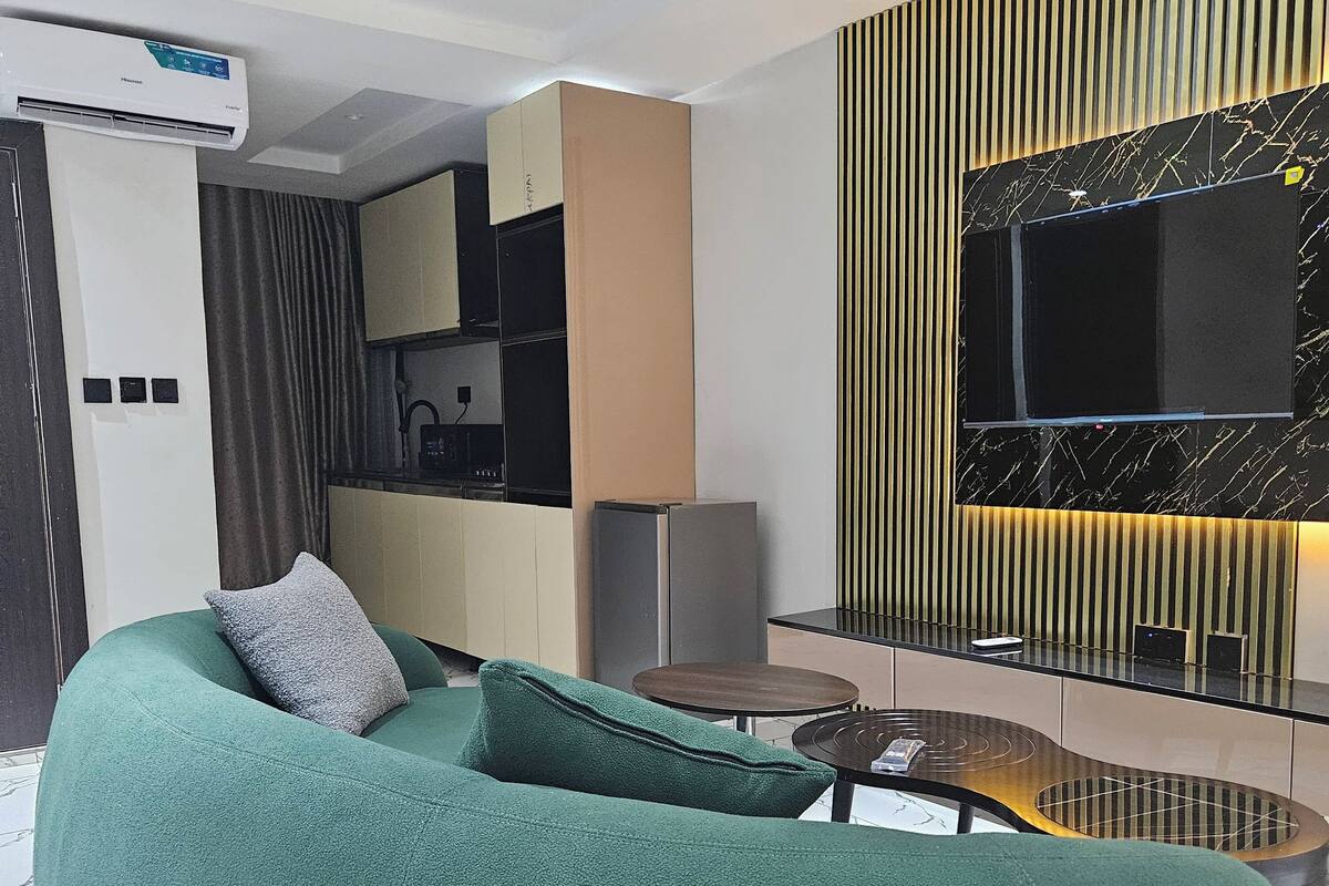 Una sala de estar moderna con un sofá verde, una mesita de centro y un televisor montado en una pared negra y dorada.