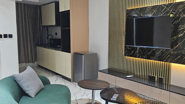 A modern living room with a green sofa, a small round table, and a built-in TV. - Anibex Luxe (Abuja)