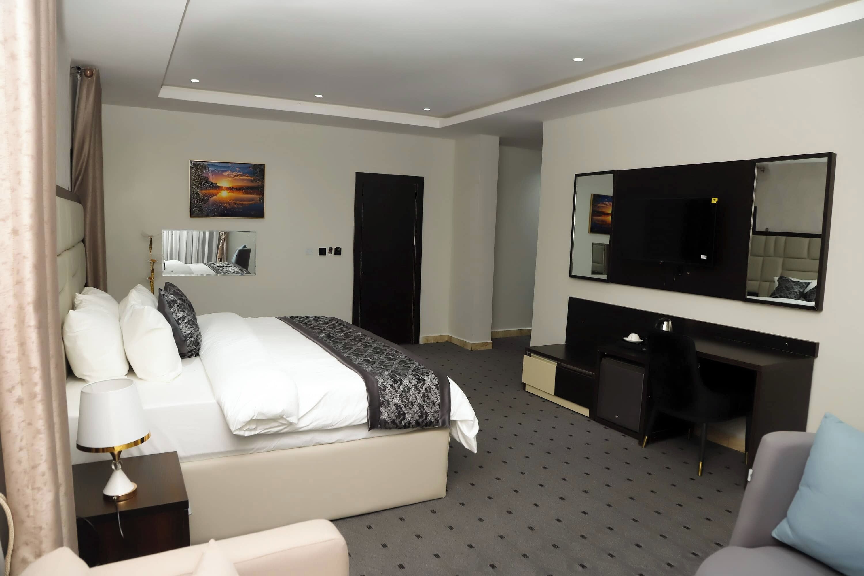 A modern hotel room with a large bed, a desk, a chair, a TV, and a painting on the wall.