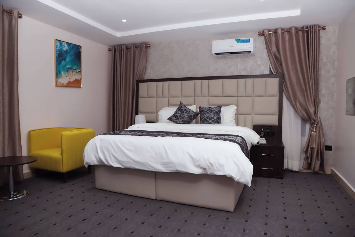 Habitación de hotel con una cama grande, una mesita de noche, una silla y un equipo de aire acondicionado en la pared.