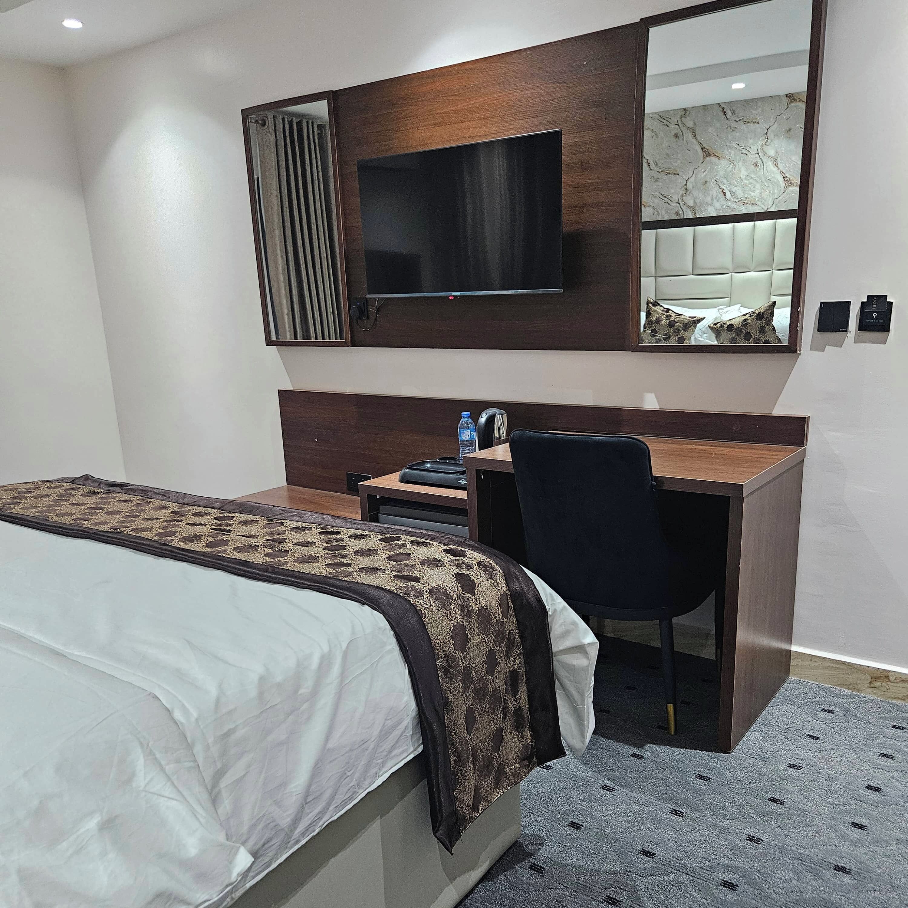 A hotel room with a bed, a desk, a chair, a television, and a mirror.