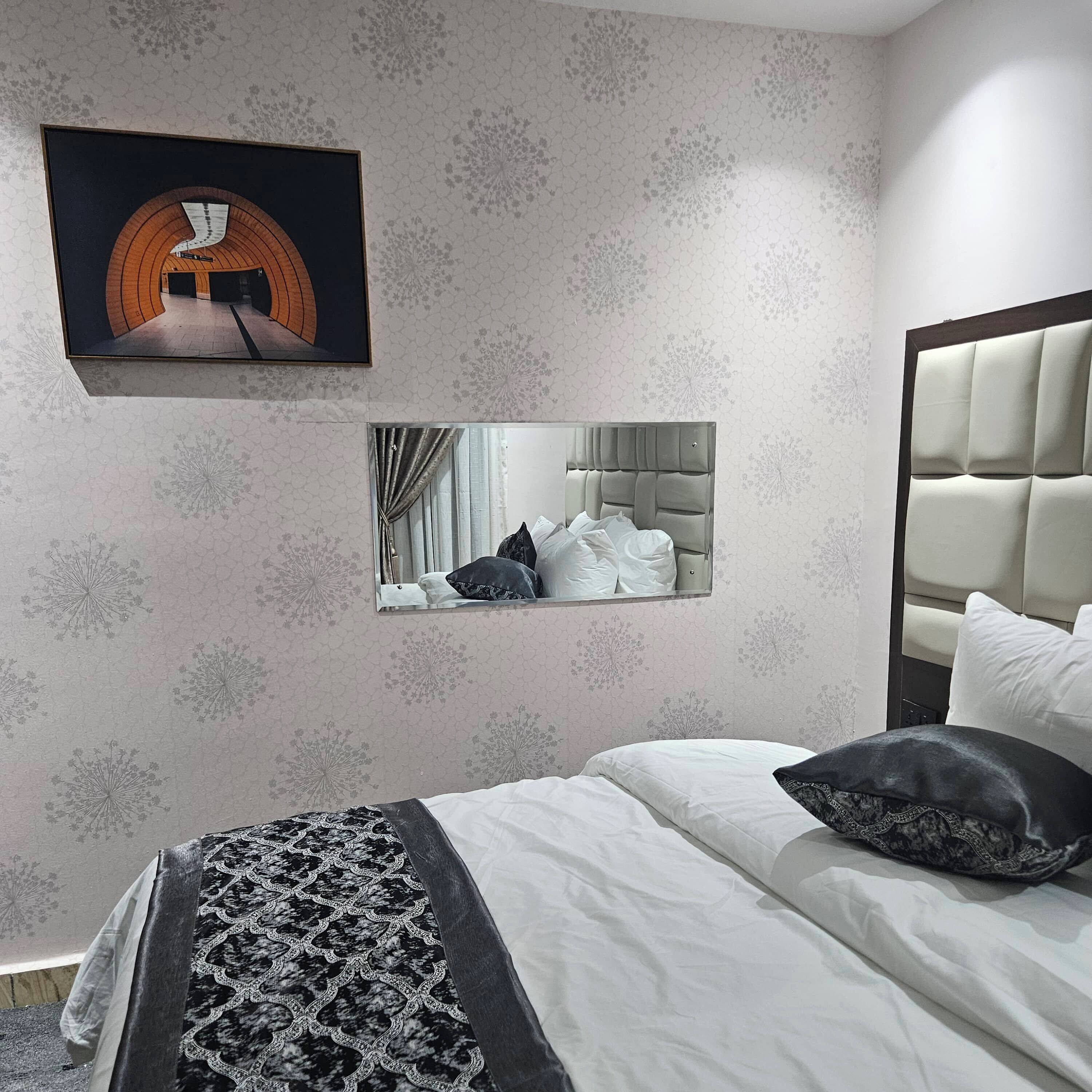 A bedroom with a bed, a headboard, a mirror, and a framed picture on the wall.