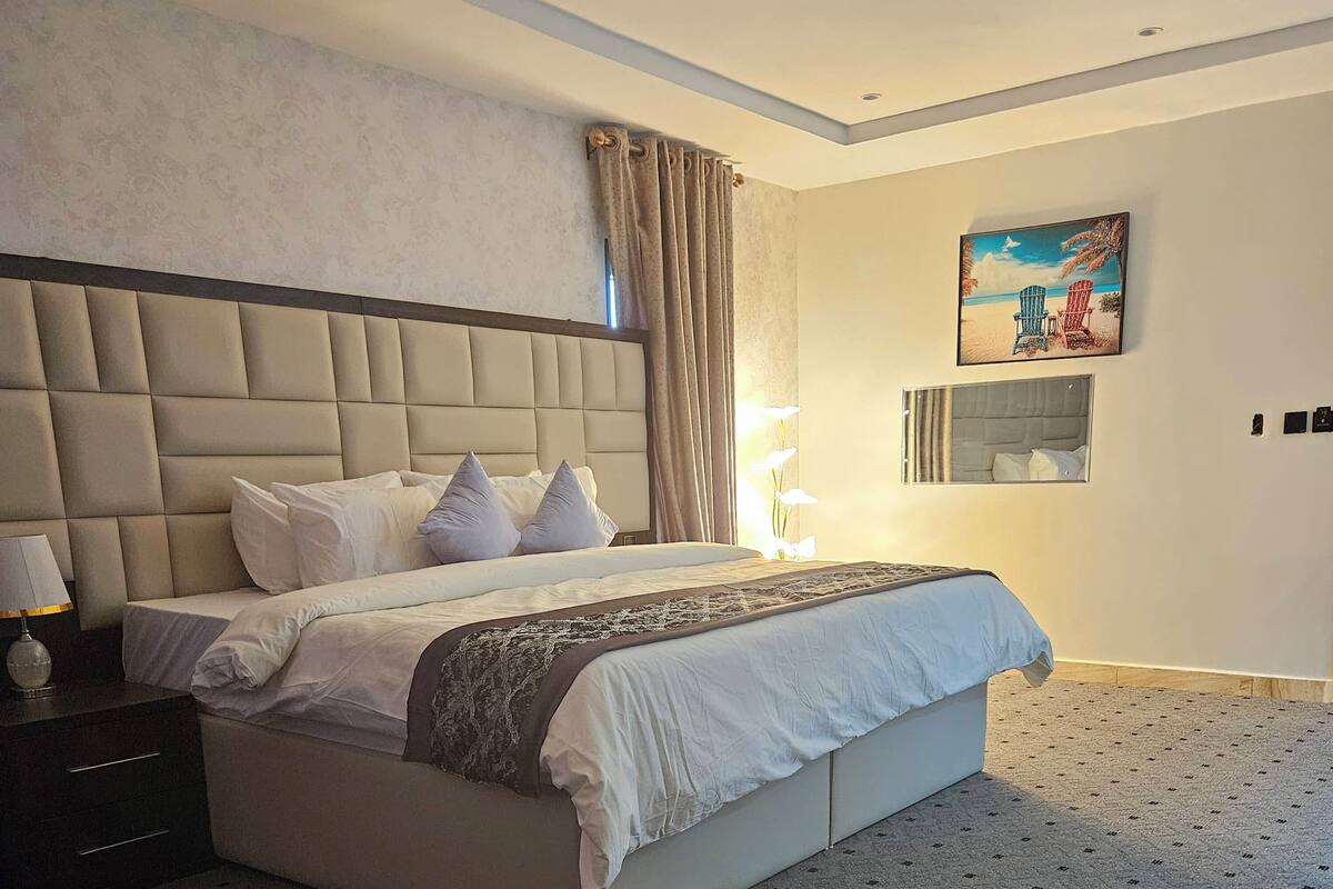 Un dormitorio con una cama grande, una mesita de noche, una lámpara y un cuadro en la pared.