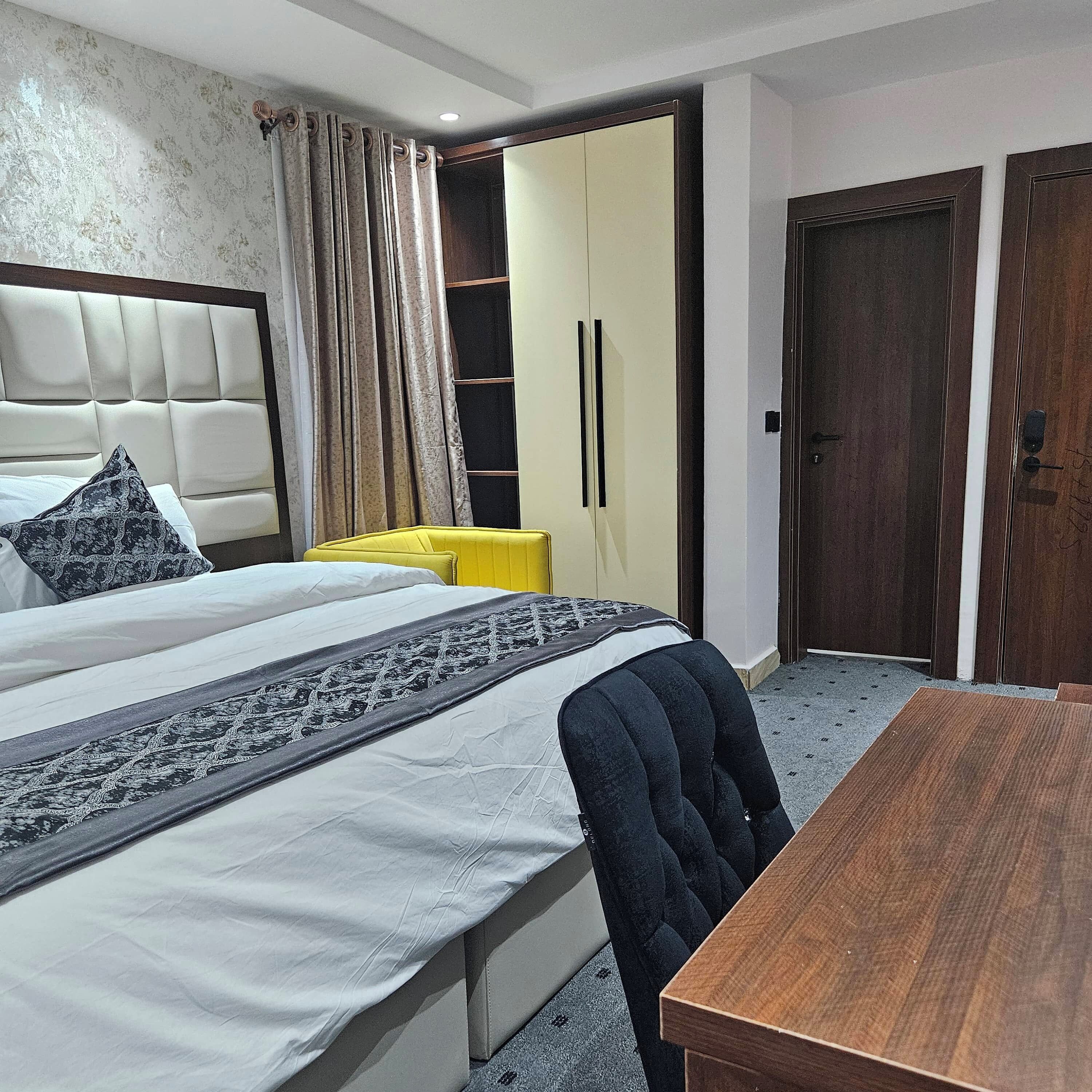 Een slaapkamer met een bed, een houten tafel, een gele stoel en een garderobe.