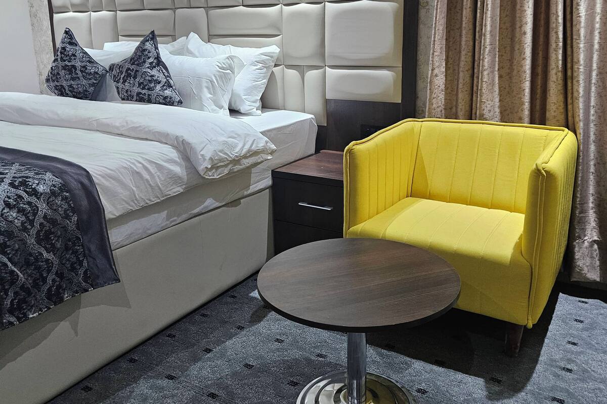 Una habitación de hotel con una cama, una mesita de noche, una silla y un equipo de aire acondicionado.