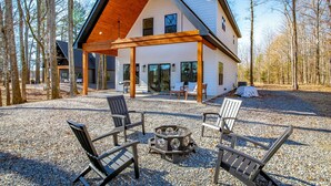 Ein modernes Haus mit einer überdachten Terrasse, Sitzgelegenheiten im Freien und einer Feuerstelle.
