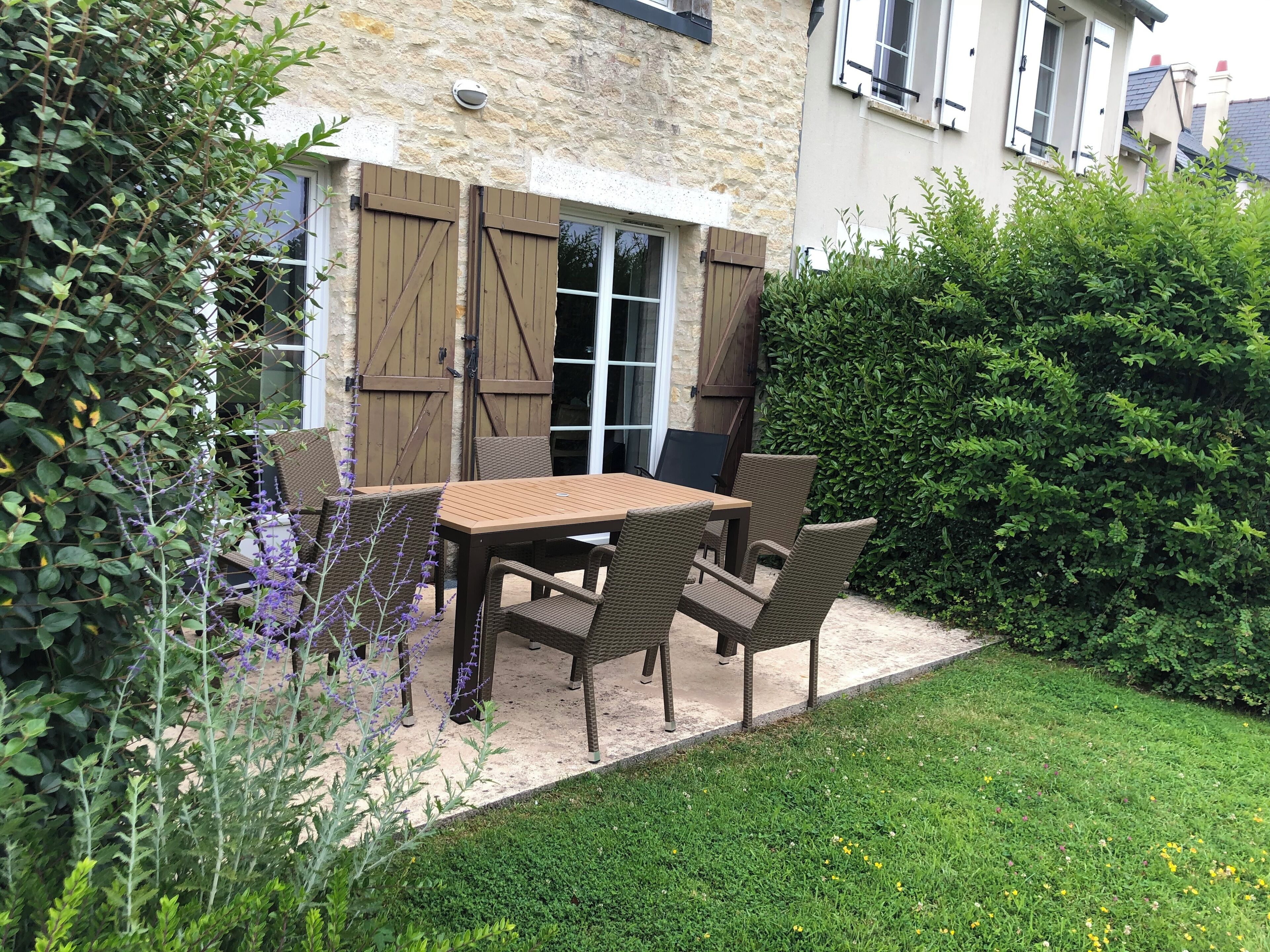 An outdoor patio with a table and chairs, surrounded by greenery and a stone building.
