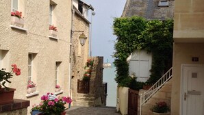 A narrow cobblestone street with stone buildings, flower boxes, and a staircase leading to a door. - Luxury living in the heart of Normandy (Port-en-Bessin-Huppain)