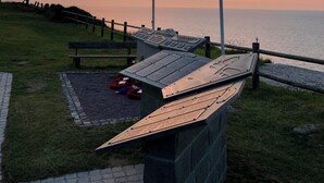 A sunset view with a flagpole, a bench, and a plaque. - Luxury living in the heart of Normandy (Port-en-Bessin-Huppain)