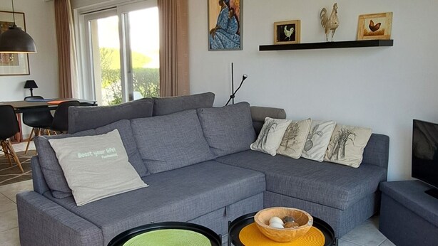 A modern living room with a grey sectional sofa, two small side tables, and a flat-screen TV.