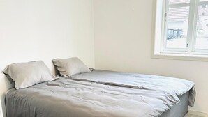 A single-bed room with a grey bedspread, a window with a view of buildings, and light-colored wooden flooring. - Apartment in the heart of Stavanger (Stavanger)