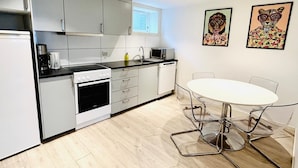 A modern kitchen with grey cabinets, a white countertop, a built-in oven, a microwave, and a sink. There's a round table with chairs and two framed artworks on the wall. - Apartment in the heart of Stavanger (Stavanger)