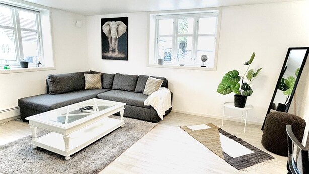 A modern living room with a sectional sofa, a glass coffee table, a large mirror, and a potted plant. - Apartment in the heart of Stavanger (Stavanger)