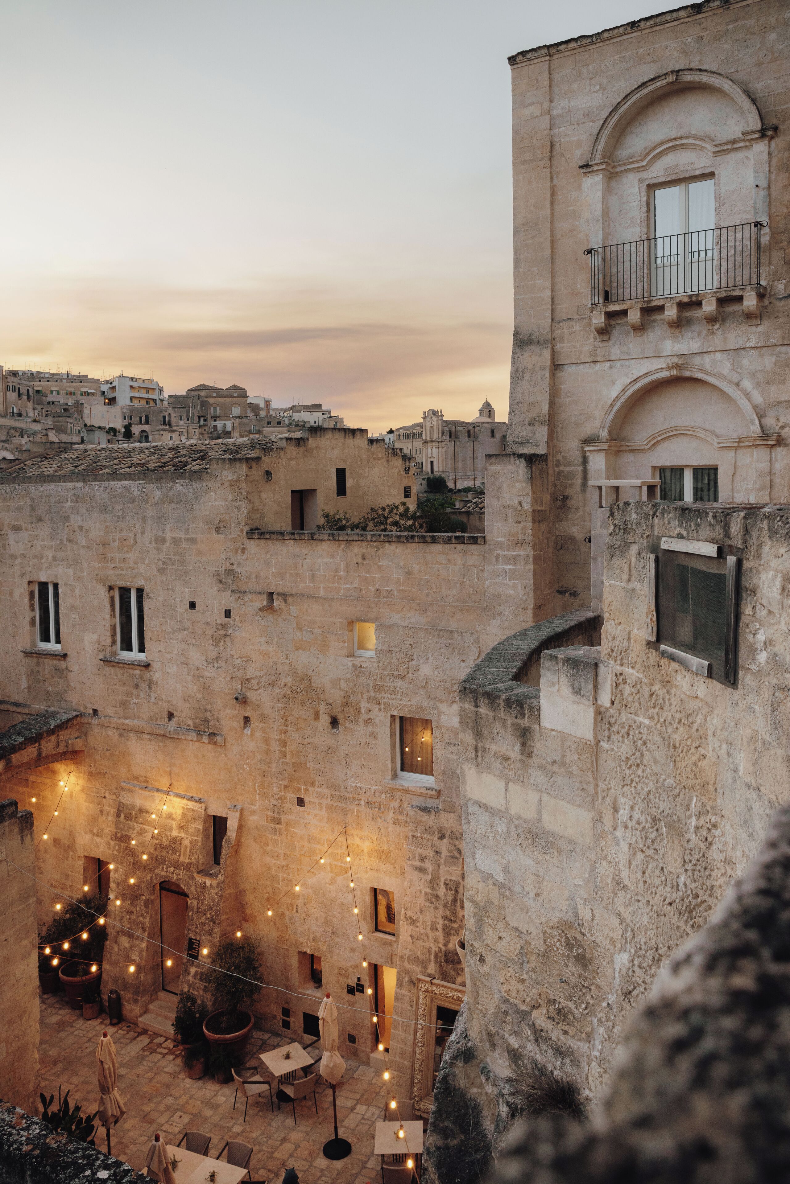 A courtyard with stone buildings, outdoor seating, and string lights.