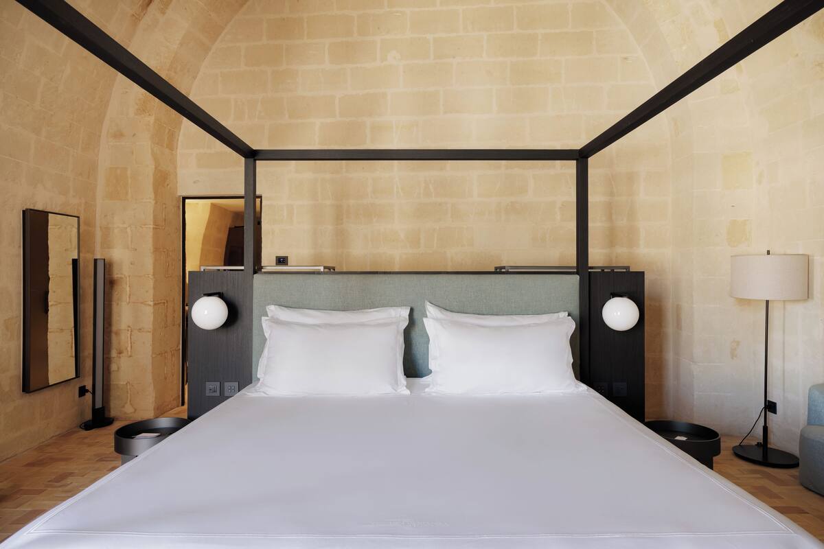 Une chambre d’hôtel moderne avec un grand lit, une tête de lit agrémentée de deux tables de chevet, une lampe et un miroir au mur.