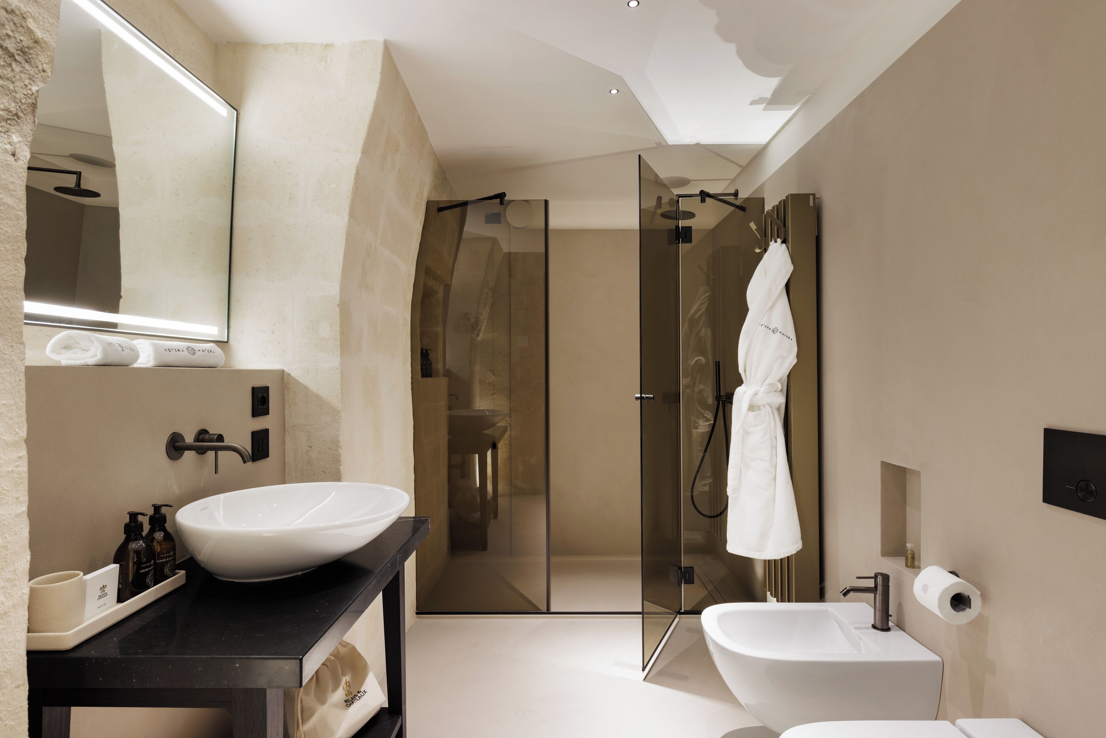 A modern bathroom with a large mirror, two sinks, a glass-enclosed shower, and a towel rack.