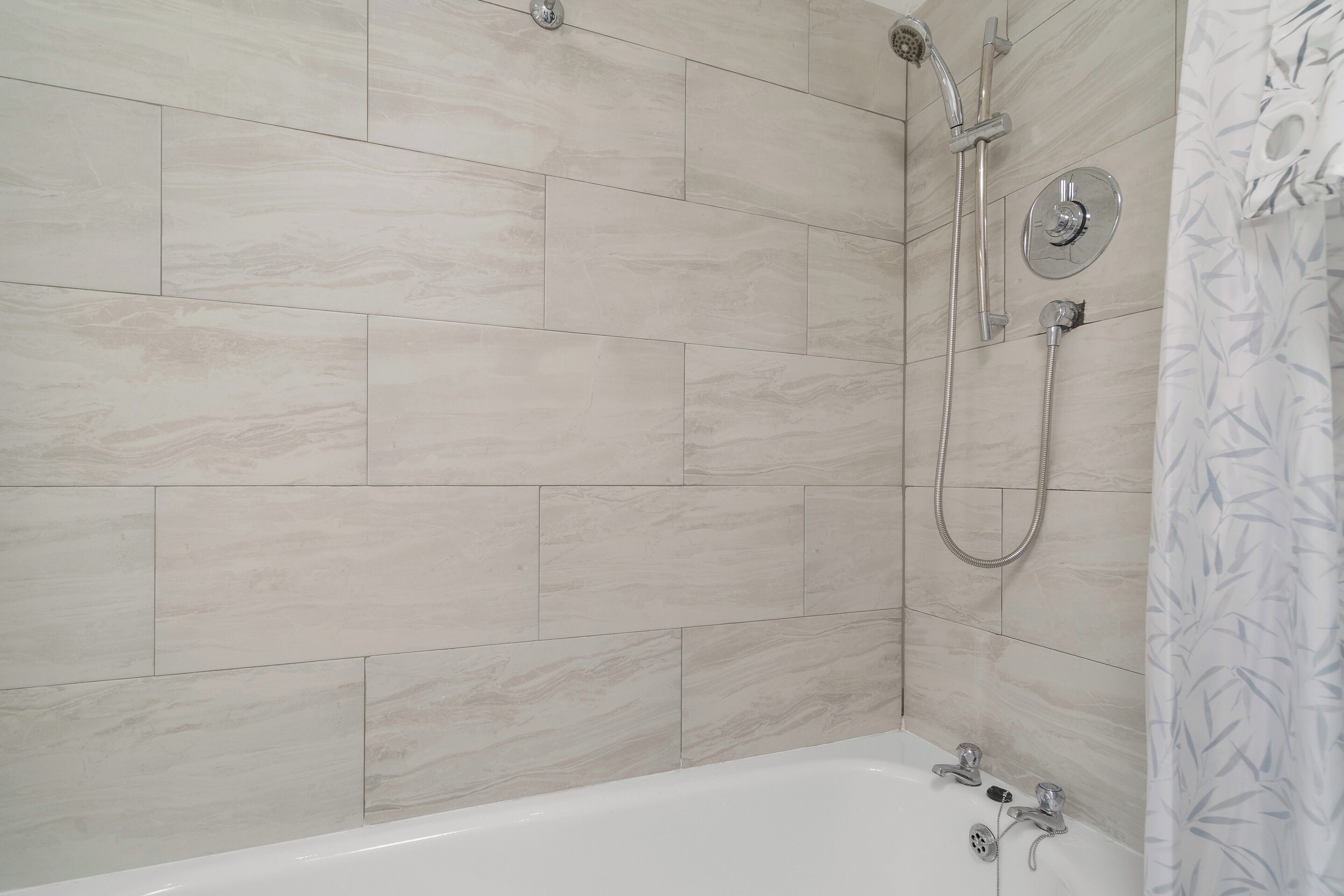 Un baño con bañera, ducha y pared de azulejos color beige.