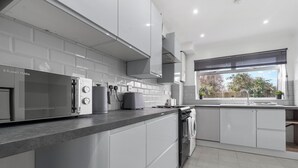 A modern kitchen with white cabinetry, a built-in oven, and a large window with blinds. - Staines House-3bed-sleeps7- Freep-close to Airport (Staines)