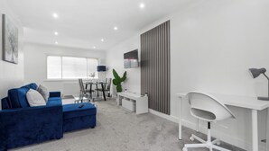 A modern living room with a blue sofa, a white desk, and a dining area. - Staines House-3bed-sleeps7- Freep-close to Airport (Staines)