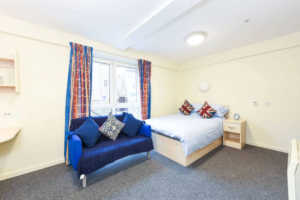 Une chambre à coucher avec un lit, un canapé bleu et une fenêtre avec des rideaux.