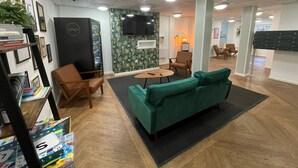 A modern office space with a green sofa, wooden chairs, a small table, and a TV on the wall. - Student Only Apollo Court (Liverpool)