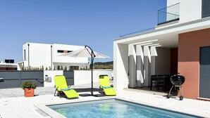 A swimming pool with two sun loungers, a barbecue grill, and a modern building with a flat roof. - Casa da Praceta - By SCH (Alfeizerão)