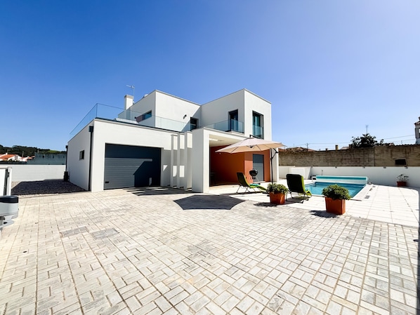 A modern two-story house with a garage, a swimming pool, and outdoor seating.