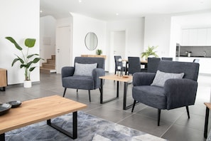 Una sala de estar moderna con sillones grises, una mesa de centro de madera y un comedor con una pequeña mesa y sillas.