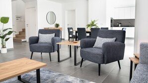 A modern living room with grey upholstered chairs, a wooden coffee table, and a dining area with a wooden table and chairs. - Casa da Praceta - By SCH (Alfeizerão)