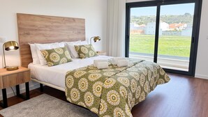 A bedroom with a large bed, a nightstand with a lamp, a view of the outdoors through a window, and a wooden headboard. - Casa da Praceta - By SCH (Alfeizerão)