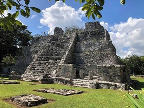 Una gran pirámide de piedra con una escalera que conduce a la cima, rodeada de zonas verdes y árboles.