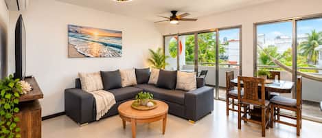 A modern living room with a sectional sofa, a coffee table, and a dining area with wooden chairs.
