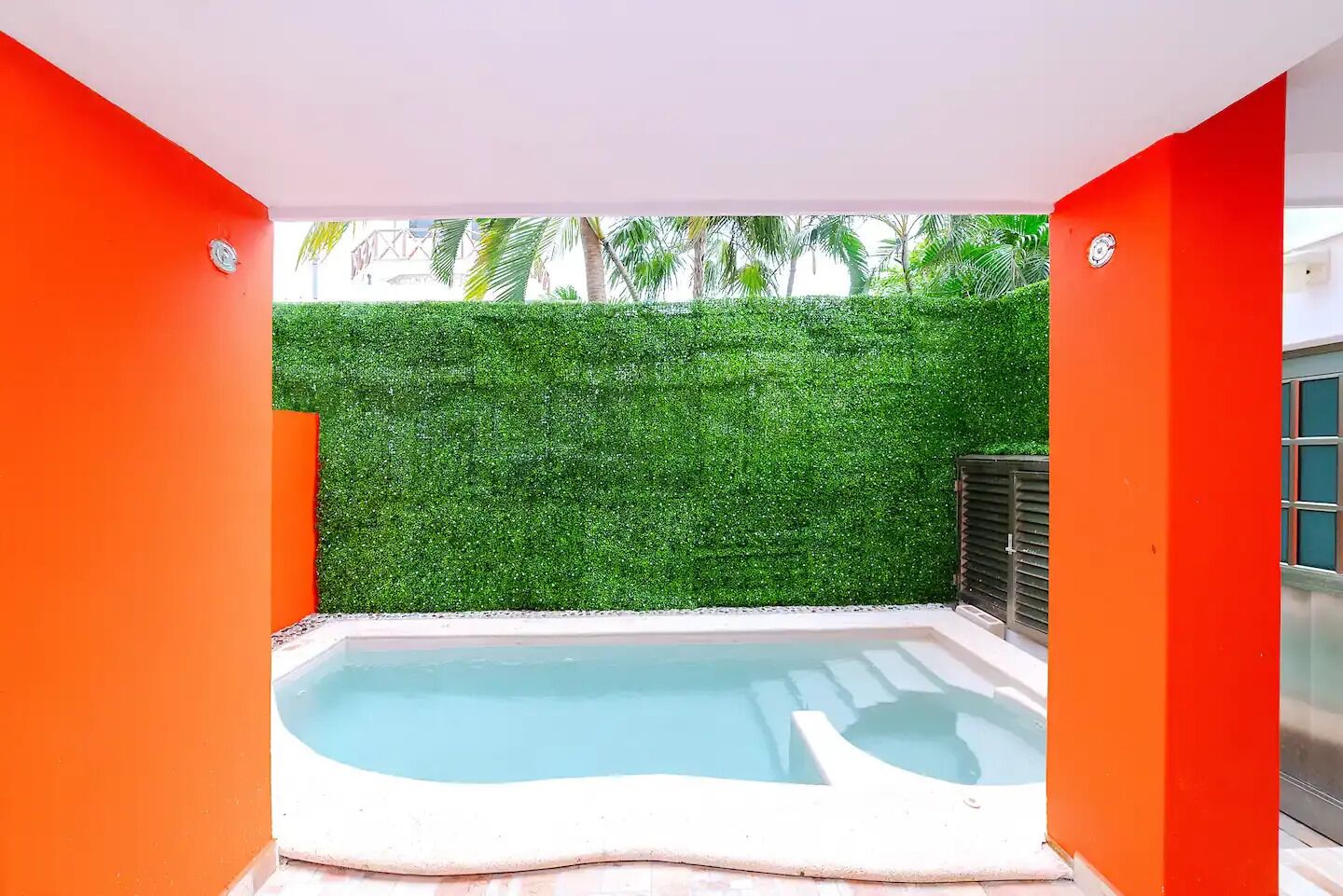 A hot tub in a modern outdoor setting with a green hedge wall and bright orange panels.