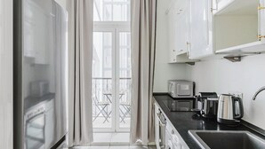 Una cocina moderna con armarios blancos, encimera negra, microondas, hervidor y fregadero.