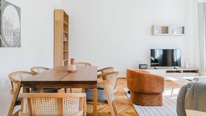 Una sala de estar moderna con una mesa de comedor de madera, sillas de mimbre, un sofá marrón y un televisor.