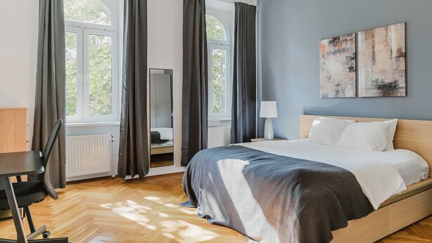 Un dormitorio con cama, escritorio, espejo y ventana con cortinas.