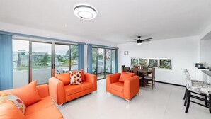 A spacious living area with orange sofas, a dining table, and a ceiling fan. - Beach Apartment#3 2BDR 1BTH in Villas Playa Blanca (Cancún)